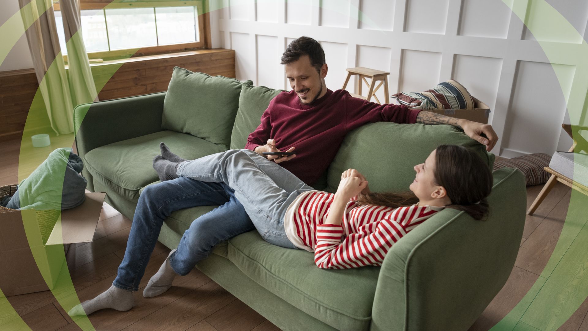 A couple relaxing on a green sofa in their new home among moving boxes